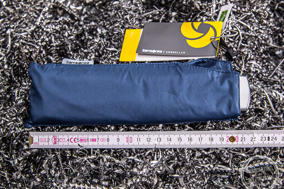 Kompakter Reiseschirm der Marke Samsonite in der Farbe Blau, in der H&uuml;lle verpackt neben einem Meterstab, um die geringe Gr&ouml;&szlig;e noch besser darzustellen.