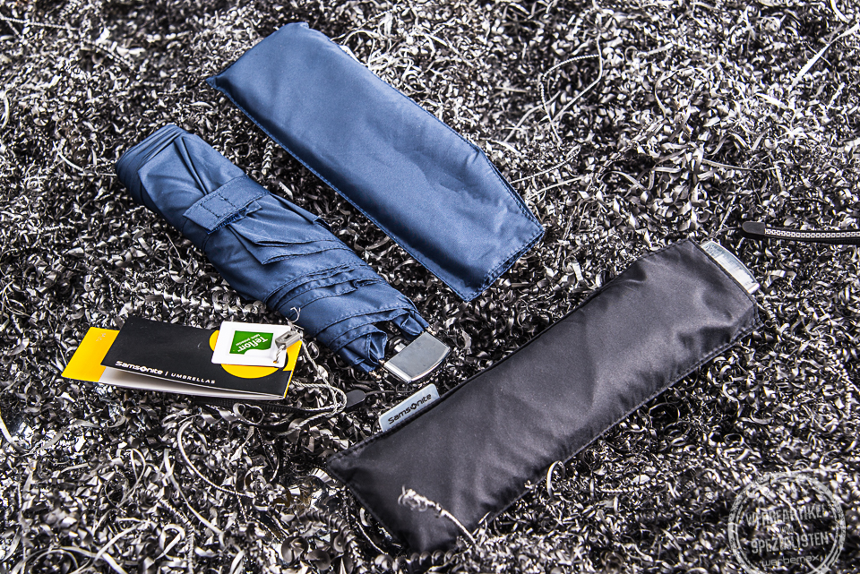 Blauer und schwarzer Samsonite Mini Taschenschirm Rain Pro liegen nebeneinander. Der blaue Taschenschirm ist aus der H&uuml;lle genommen