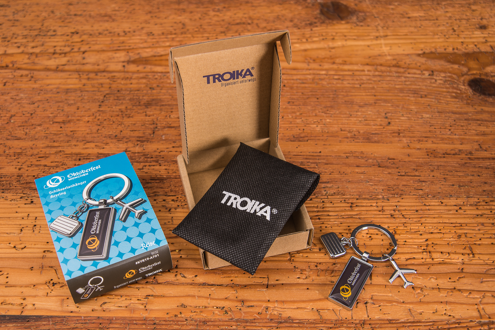 Troika Oktoberfest Schl&uuml;sselanh&auml;nger mit Koffer und Flugzeug Symbol sowie Oktoberfest Logo pr&auml;sent in der Mitte.