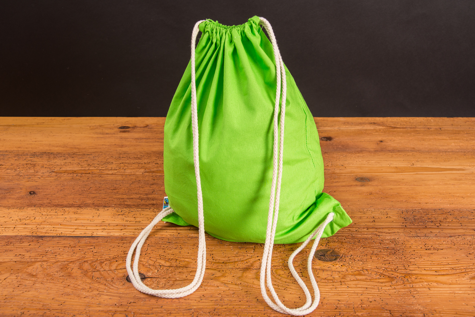 Baumwollrucksack Hanna in Hellgr&uuml;n stehend auf einem Holztisch mit naturfarbenen Baumwollkordeln