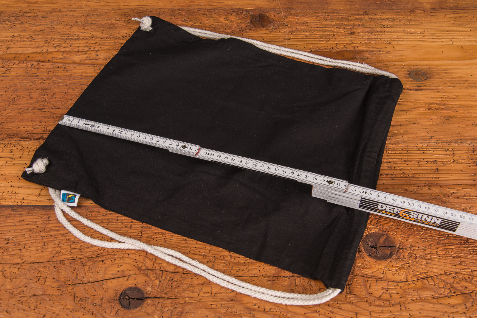 schwarzer Matchrucksack aus Fairtrade Baumwolle mit naturfarbenen Baumwollkordeln. Ein Meterstab zeigt die genaue H&ouml;he des Turnbeutels. 