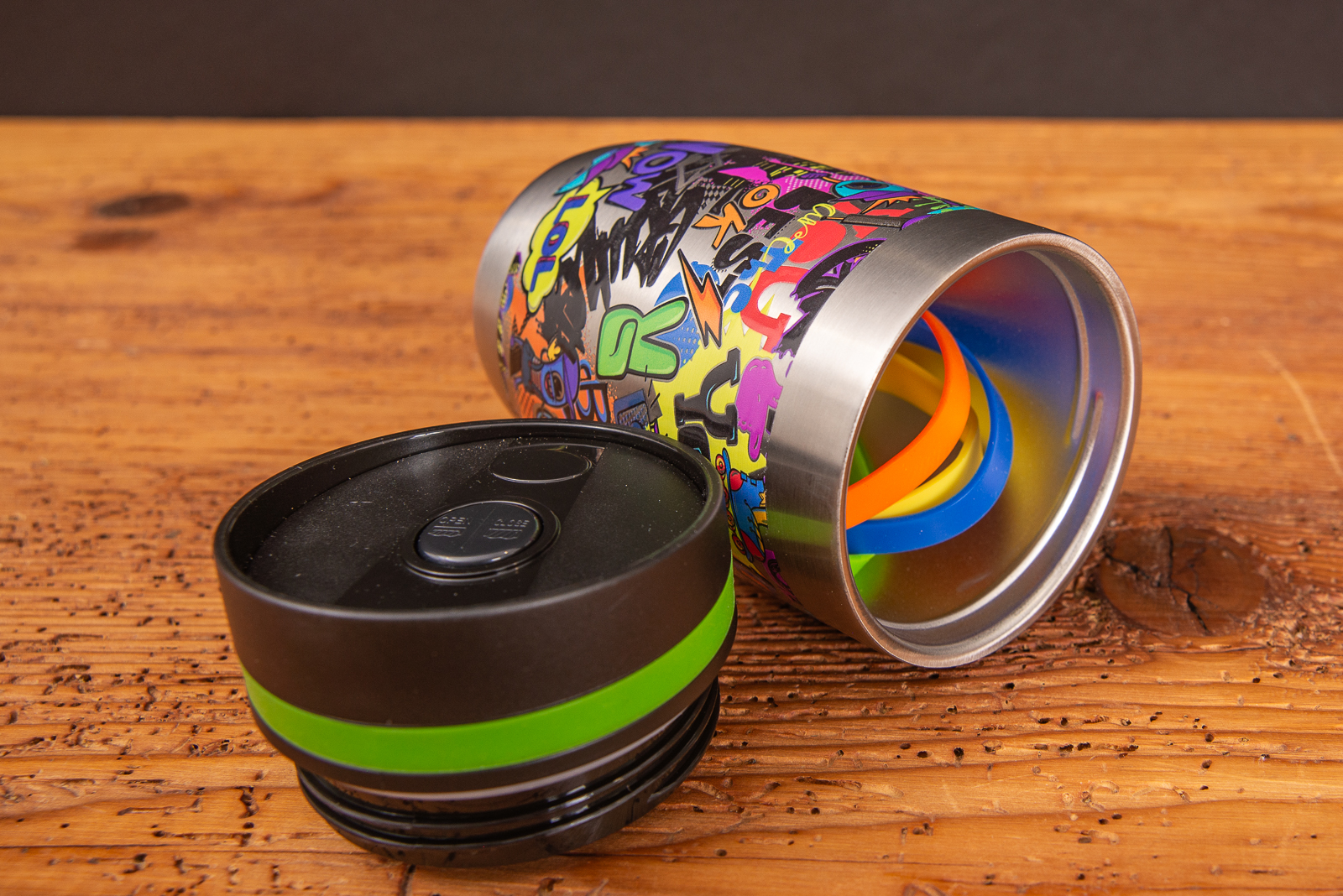 Bedruckter Thermobecher liegend mit abgeschraubtem Deckel und austauschbaren Gummiringen als Werbeartikel.