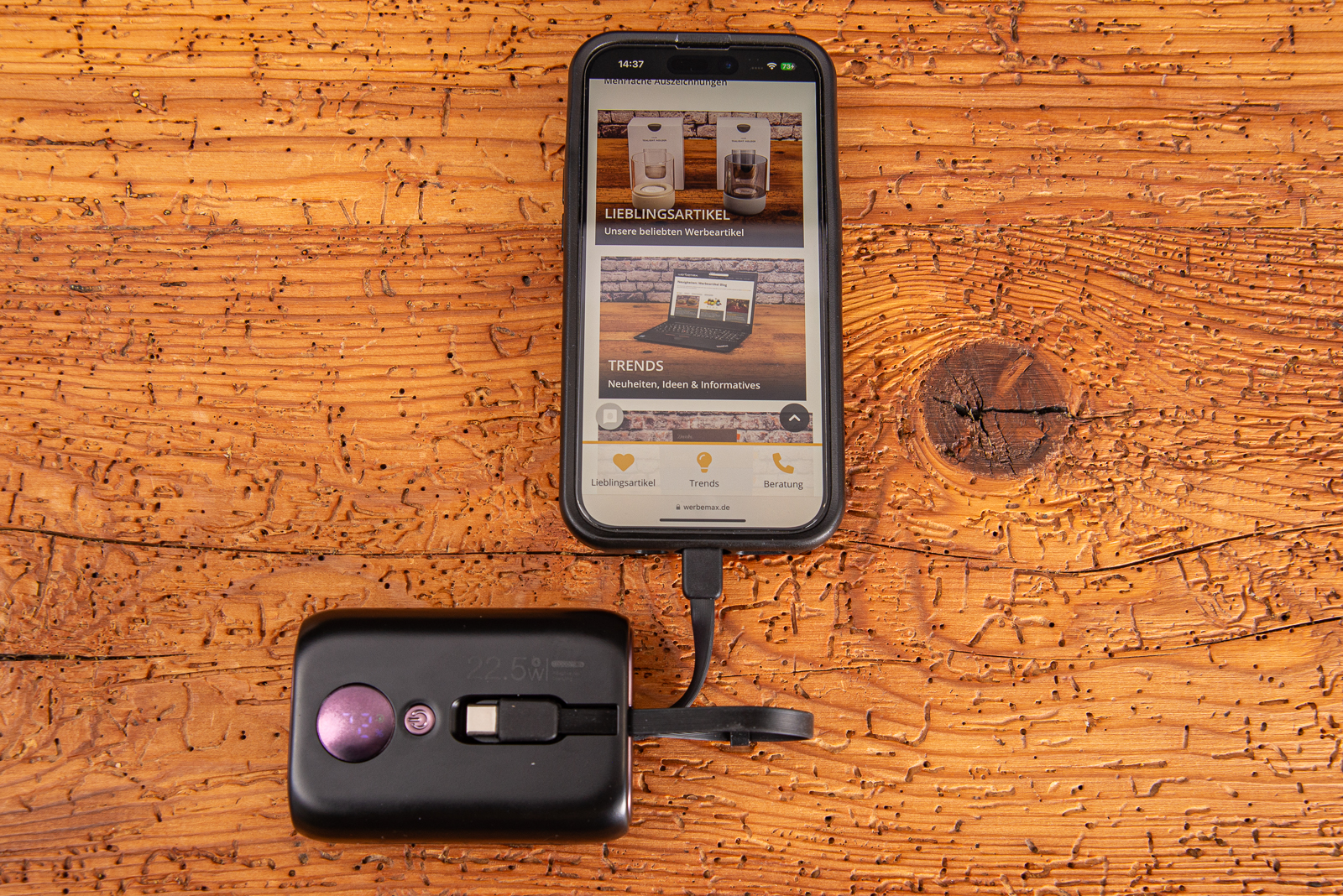 Schwarze 10.000 mAh Powerbank mit Ladestandsanzeige mit einem angeh&auml;ngten Apple iPhone.