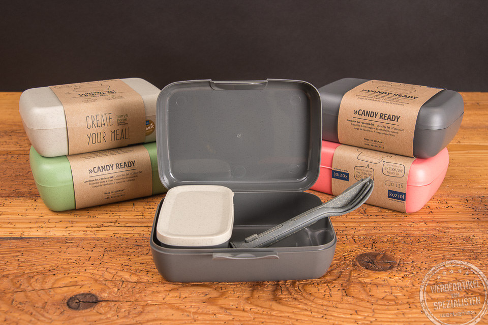 Mehrere koziol Brotdosen in unterschiedlichen Farben mit Werbebanderole und Besteck-Set.