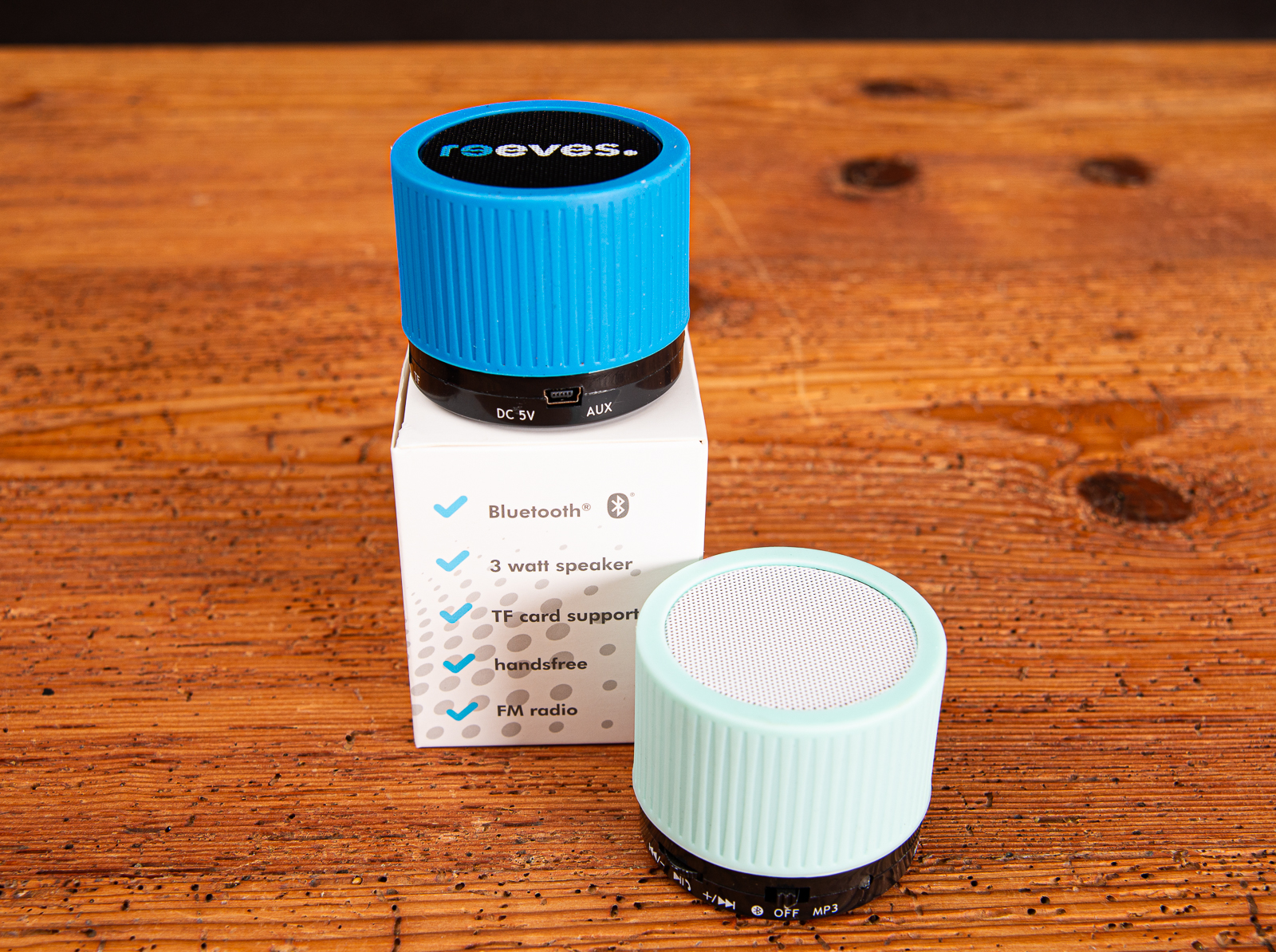 Ein schwarzer und ein wei&szlig;er Bluetooth Speaker mit buntem Gummiring als Merch auf Holzplatte.