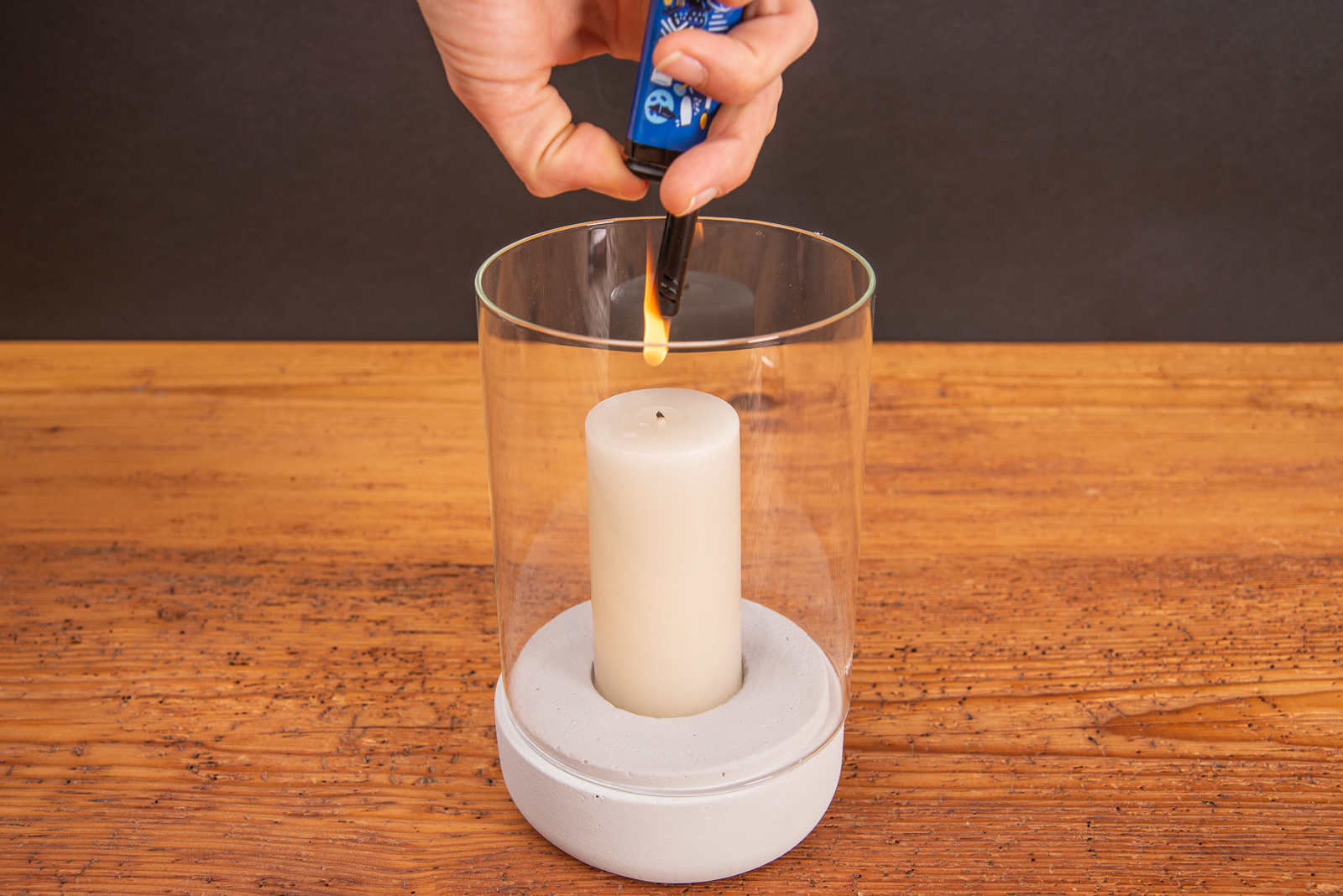 Eine Windlicht, dessen Kerze mit einem Werbe-Stabfeuerzeug angez&uuml;ndet wird.