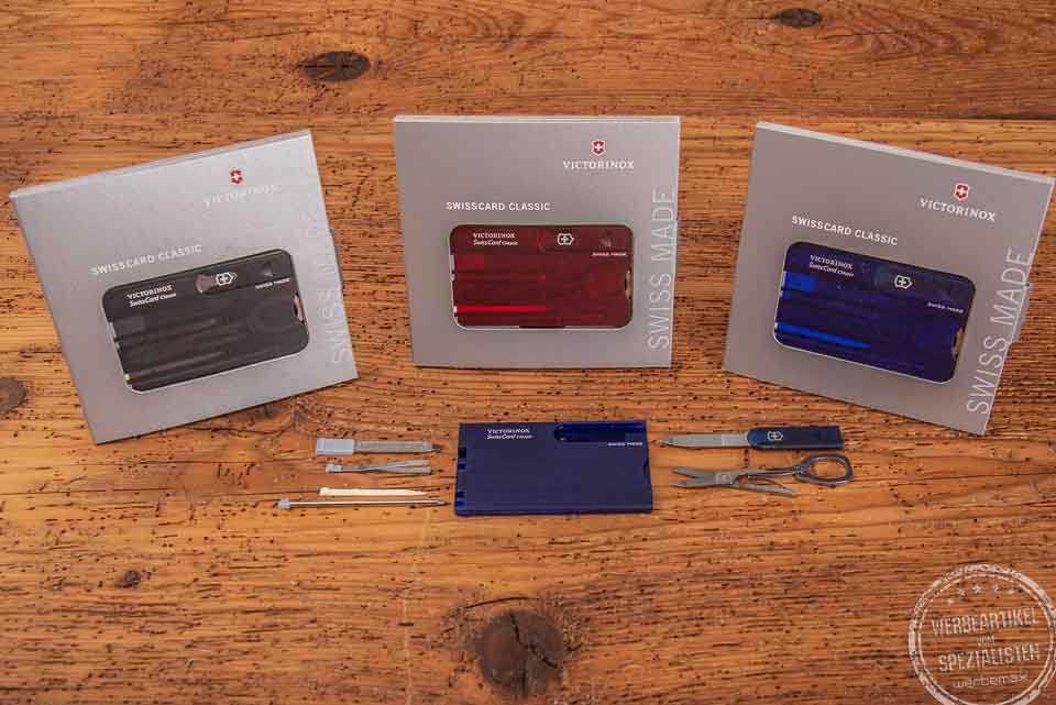 Vier unterschiedlich farbige SwissCards von Victorinox liegend auf einer Holzplatte als Werbeartikel.