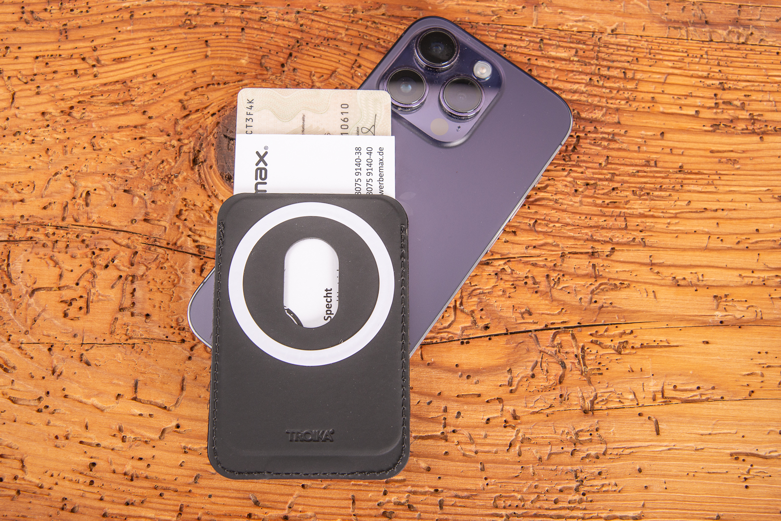 Kartenetui mit MagSafe Technologie als hochwertiges Merch f&uuml;r Mitarbeiter und Kunden aus Kunstleder von der Marke Troika f&uuml;r 1-2 Karten mit Handy auf Holztisch liegend