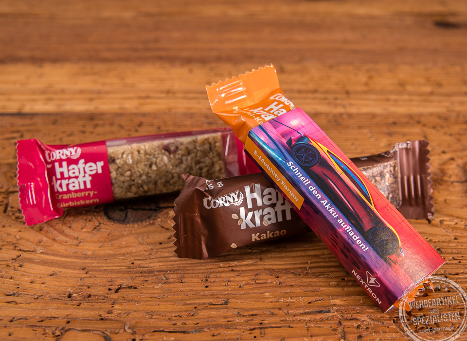 Corny Haferkraft Riegel als Give-away auf Messen im individuell bedruckten Kartonschuber auf Holztisch.