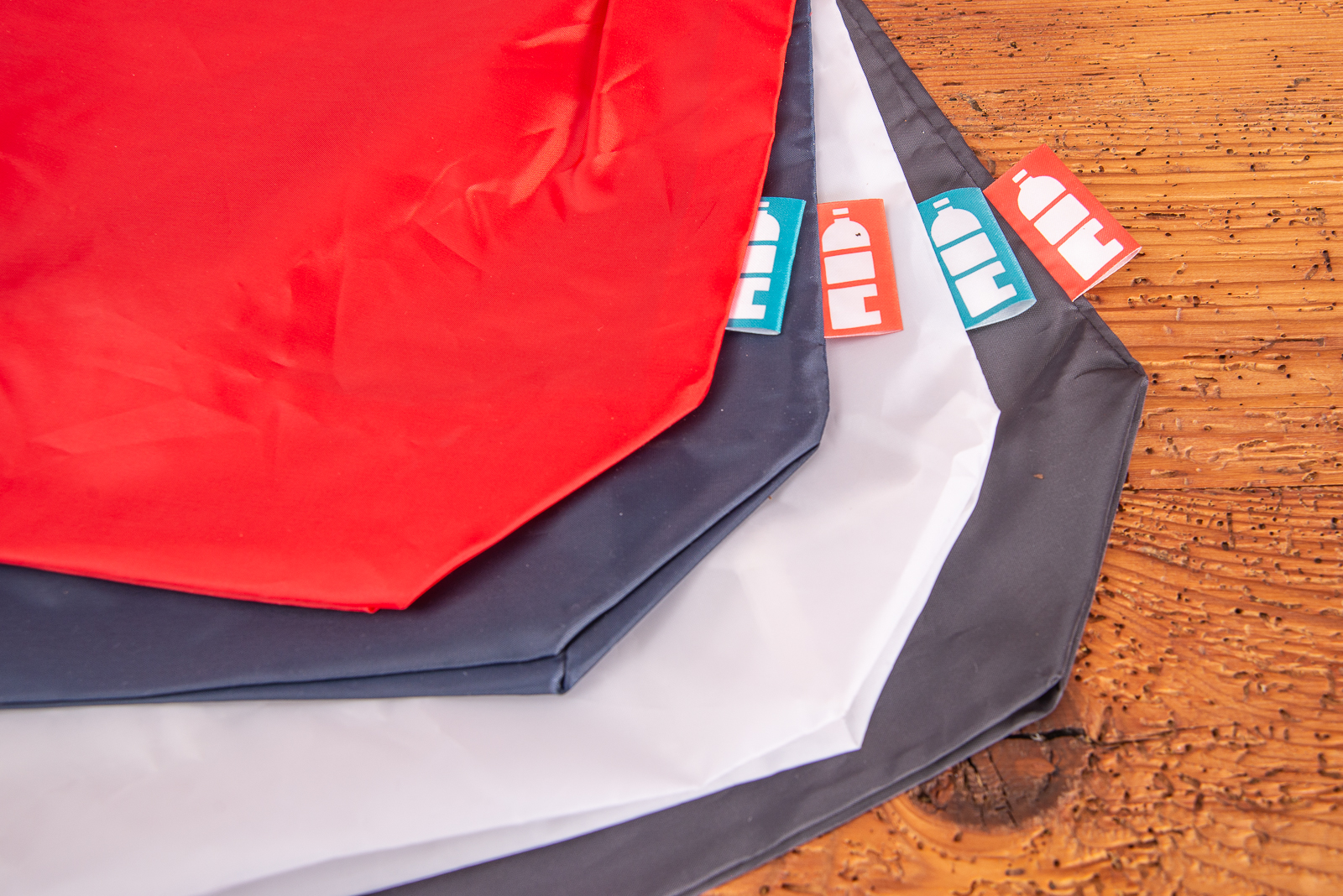 Faltbare Einkaufstaschen aus 100% recycelten PET Flaschen. Nachhaltige Werbegeschenke mit Ihrem Logo bedrucken in 4 Farben &uuml;bereinander liegend auf Holztisch