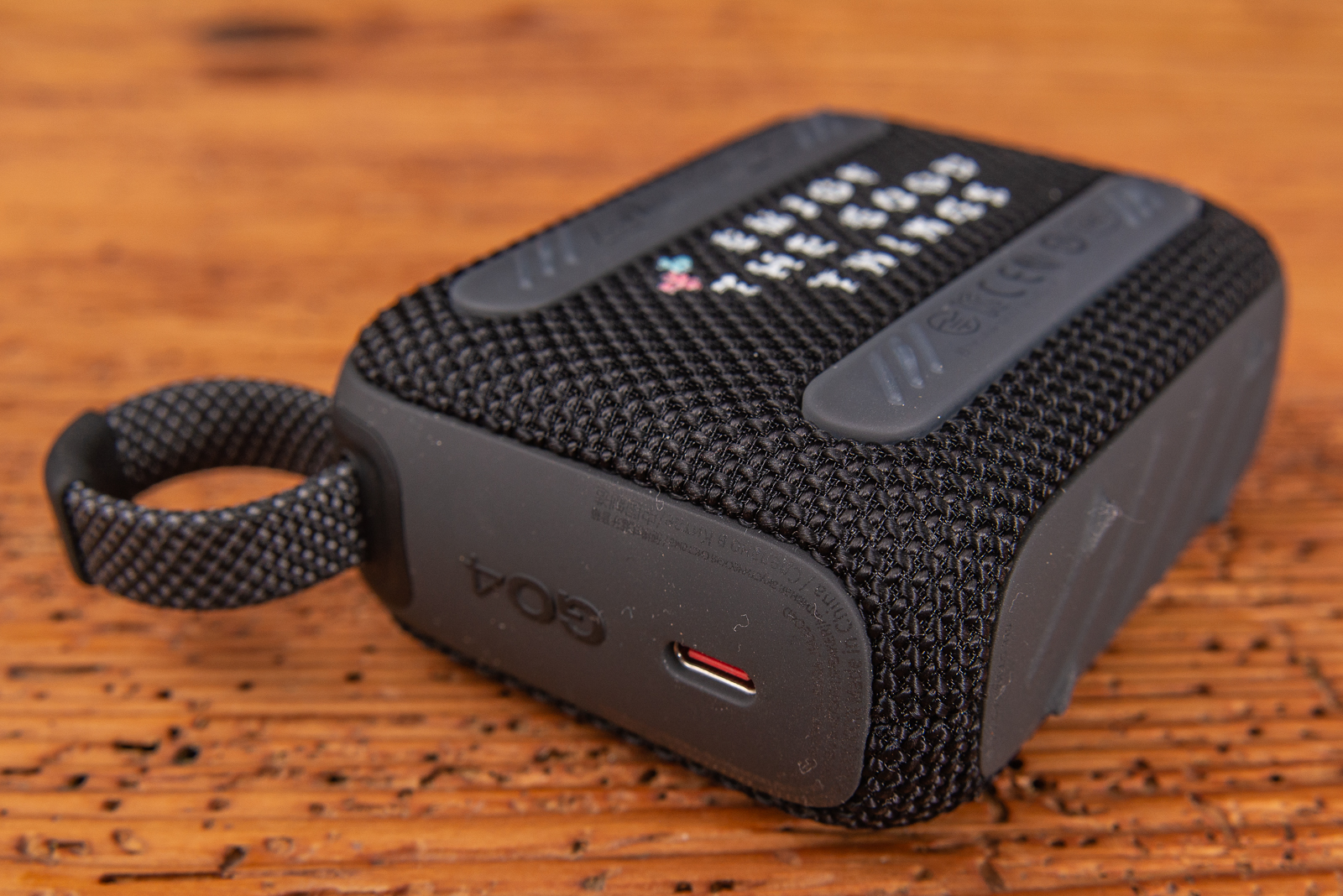 Schwarzer JBL GO 4 Bluetooth Speaker mit Logodruck als Merch auf Holzplatte liegend.