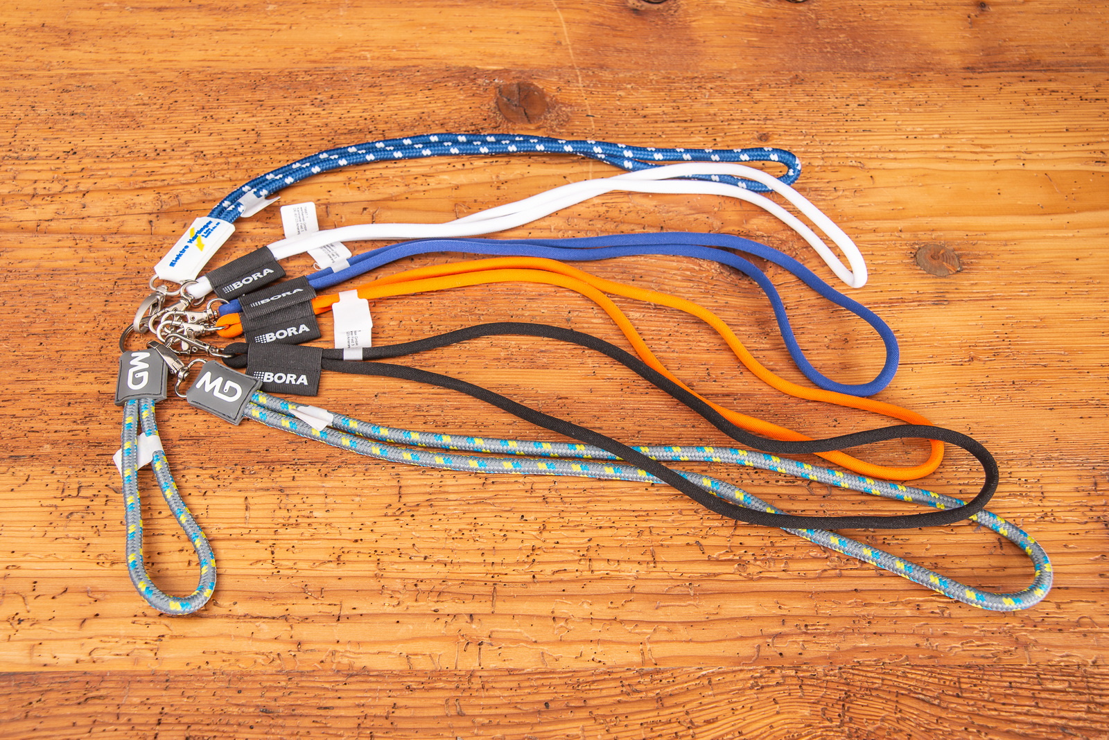 Sieben unterschiedliche Kordel-Lanyards mit Silikon-Patch Logo als Werbeartikel, das in keinem Marketingprogramm fehlen darf auf Holzplatte.