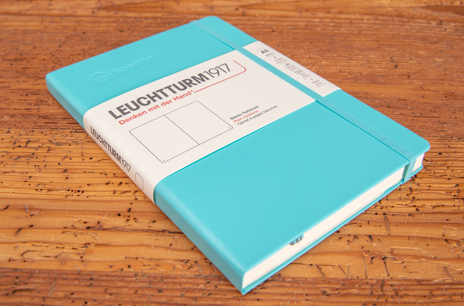 Leuchtturm1917 Notizbuch t&uuml;rkis mit Pr&auml;gung liegend auf Holztisch.