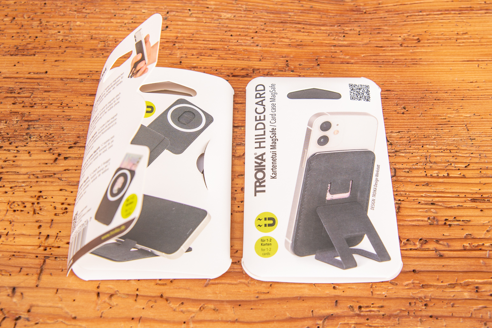 Das praktische Incentiv ist Handyhalter und Kartenetui mit MagSafe und &uuml;berzeug durch veganes Leder und einer Kartonverpackung auf Holztisch liegend