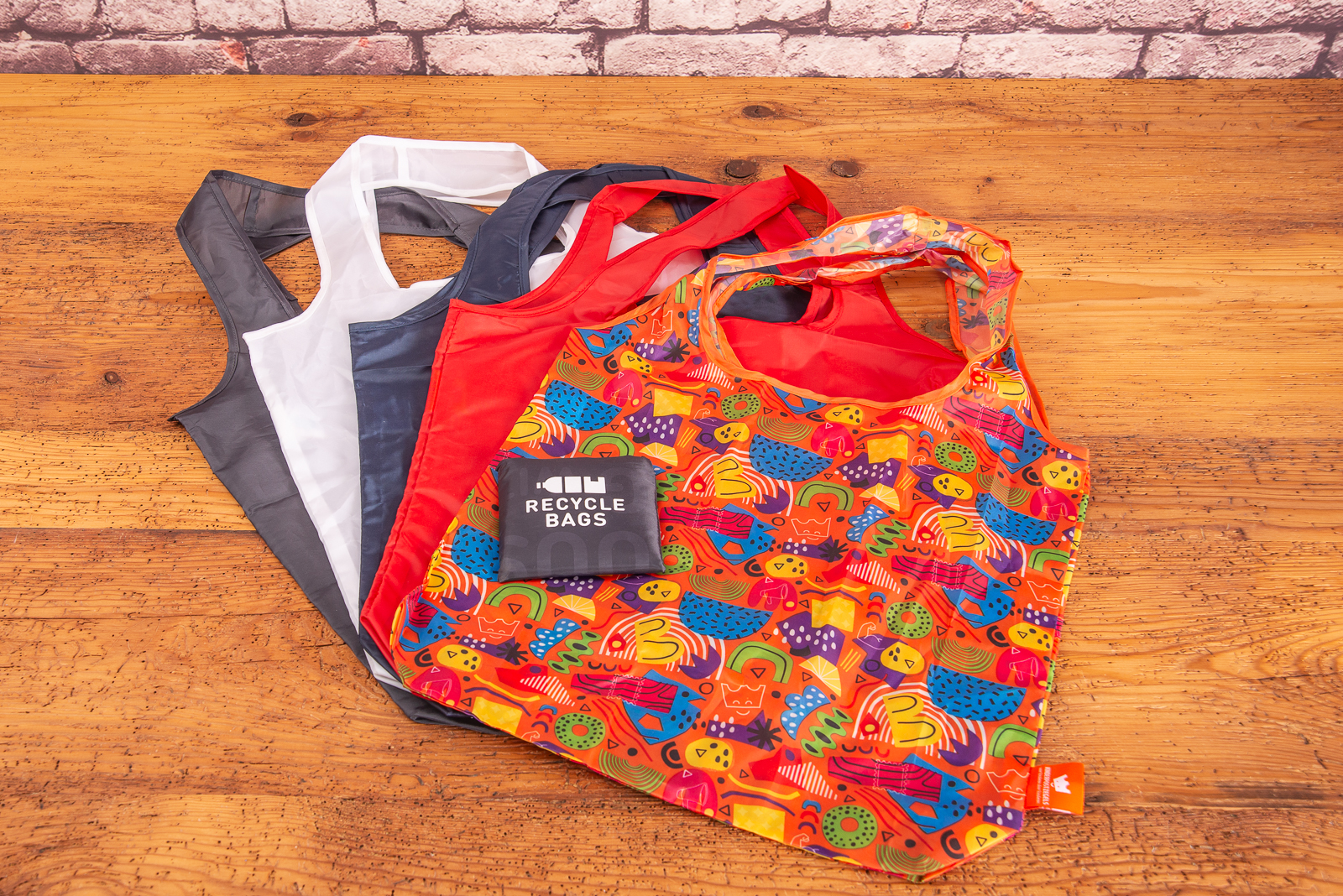 Nachhaltige Einkaufstasche aus recycelten Plastikflaschen mit Logo bedruckbar als Werbegeschenk f&uuml;r umweltbewusste Unternehmen &uuml;bereinander liegend auf Holztisch.