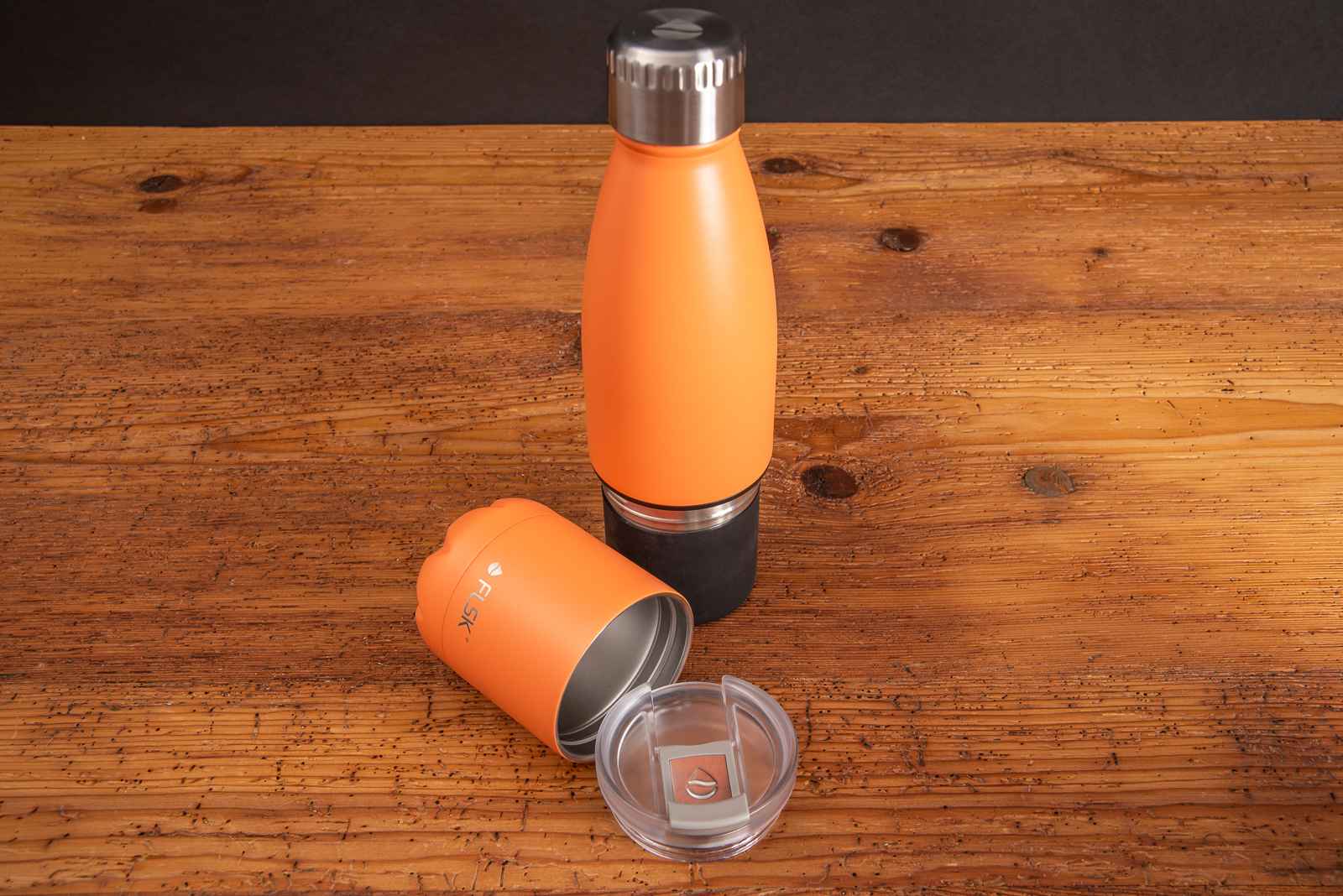 Orange Isolierflasche von FLSK mit abnehmbaren Becher und auflaufsicherem Deckel las Incentive auf Holztisch. 
