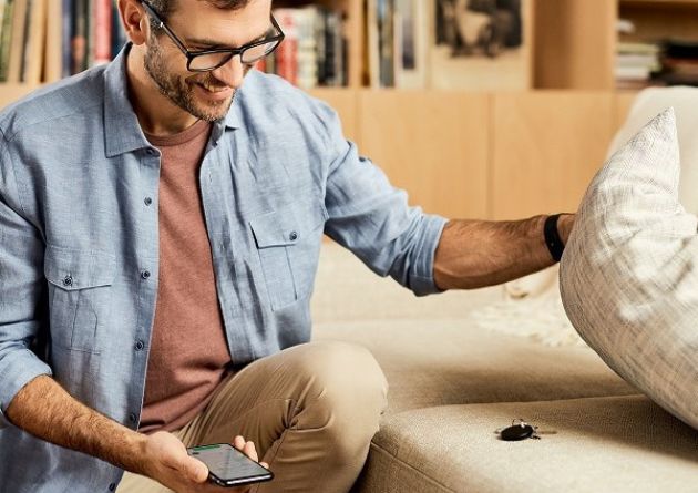 Hochwertiges Werbegeschenk - Key Finder Chipolo in schwarz auf Sofa unter Kissen.