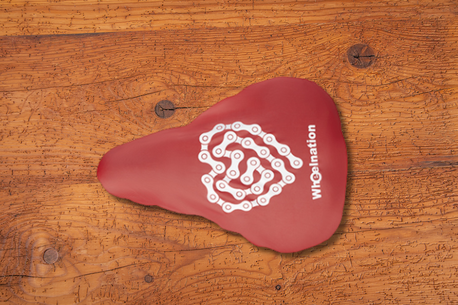 Roter Sattelschoner mit Logodruck als Werbegeschenk auf Veranstaltungen und Events auf Holzplatte.