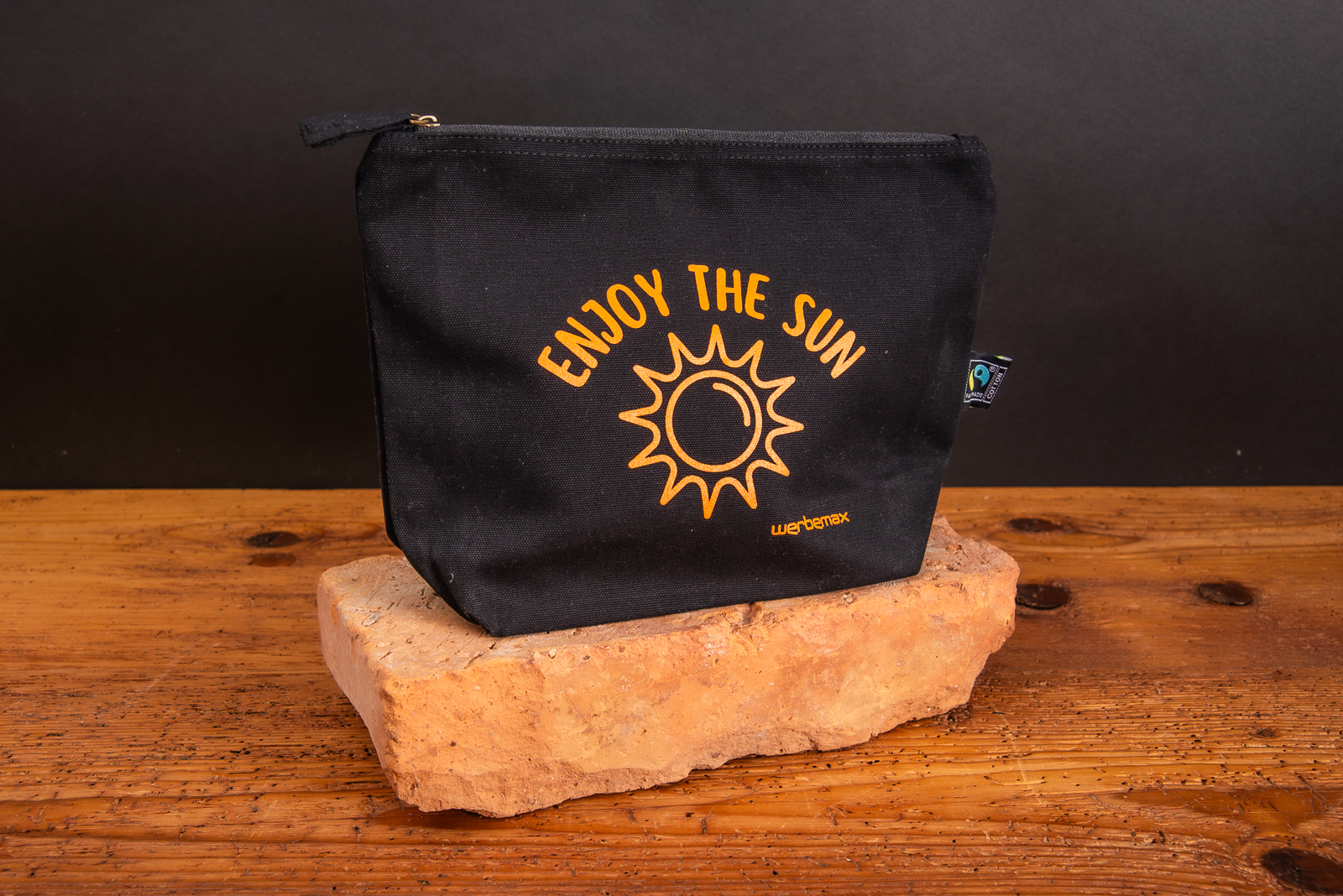 Schwarze Kosmetiktasche KYLIE mit Logodruck orange als Eigenwerbung werbemax auf Backstein stehend.