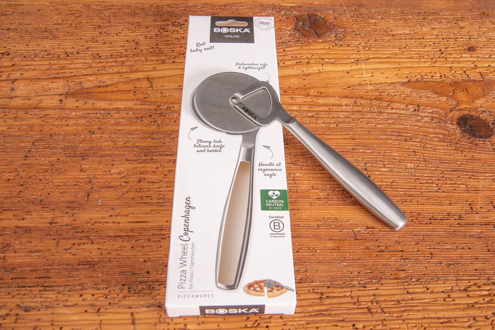 Mitarbeitergeschenk Pizzaroller Boska in einer sch&ouml;nen Kartonverpackung. Mit Lasergravur als langlebiger Werbeartikel unverzichtbar in jeder K&uuml;che. Auf Holztisch