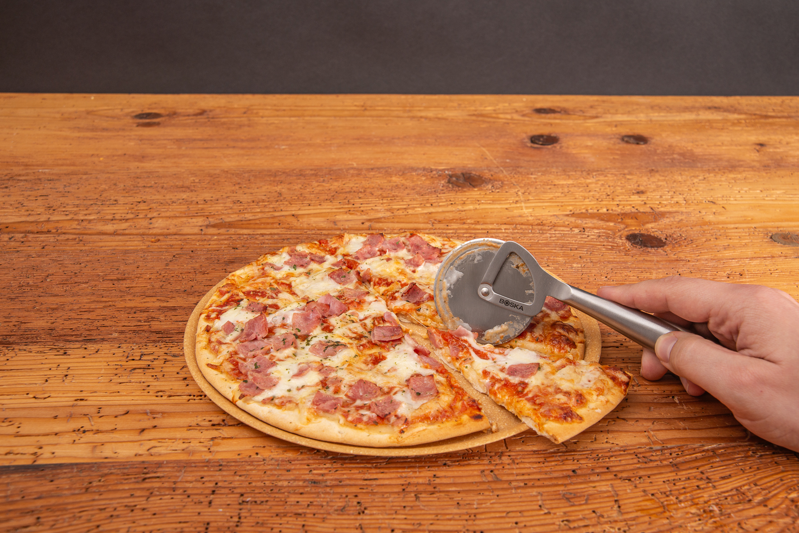 Hochwertiger Pizzaroller mit Lasergravur als Mitarbeitergeschenk auf Holztisch. Pizzaroller schneidet eine frische Pizza. 
