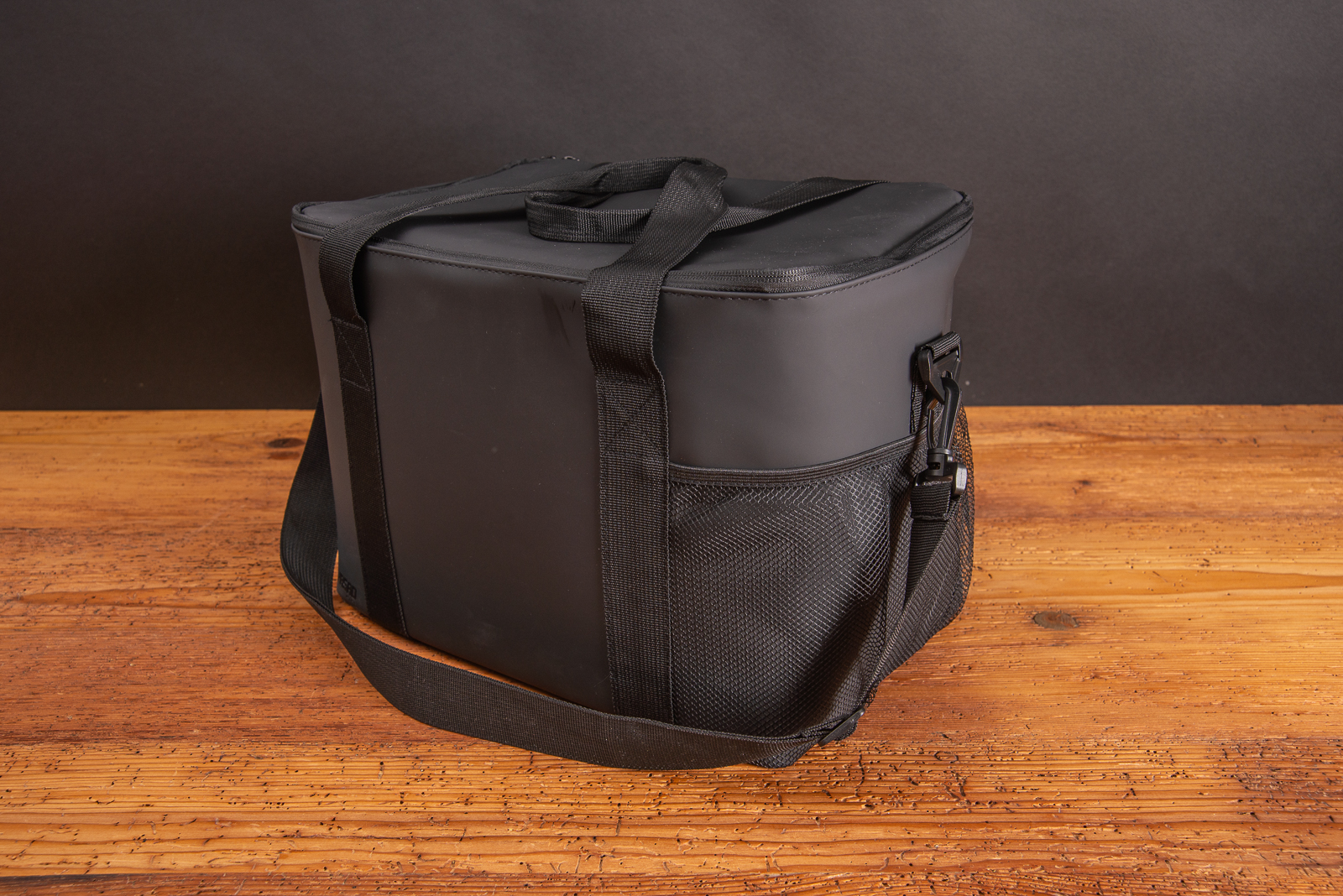 Ger&auml;umige K&uuml;hltasche aus schwarzem PU-Leder mit gro&szlig;em Innenfach f&uuml;r bis zu 15 Bierflaschen, Verpflegung f&uuml;r einen Tagesausflug und gro&szlig;er Werbefl&auml;che f&uuml;r Ihr Logo auf Holztisch