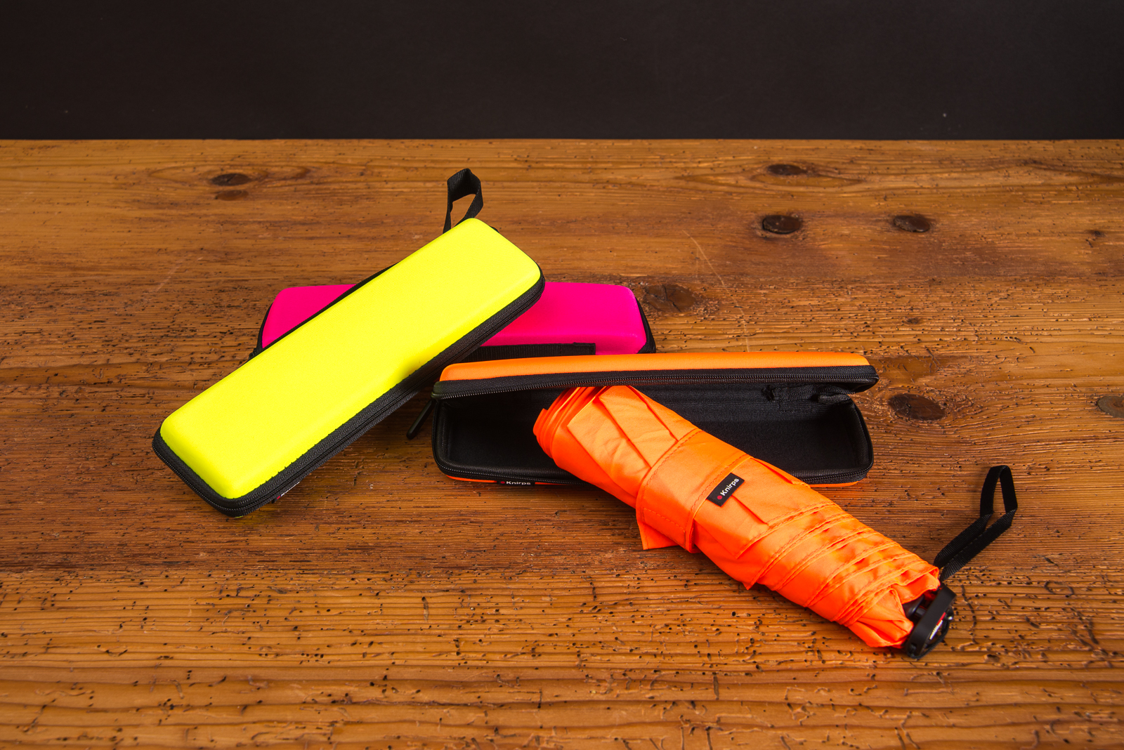 Regenschirm mit Logo von Knirps in gelb, pink und offen in neonorange auf Holztisch als perfektes Mitarbeitergeschenk