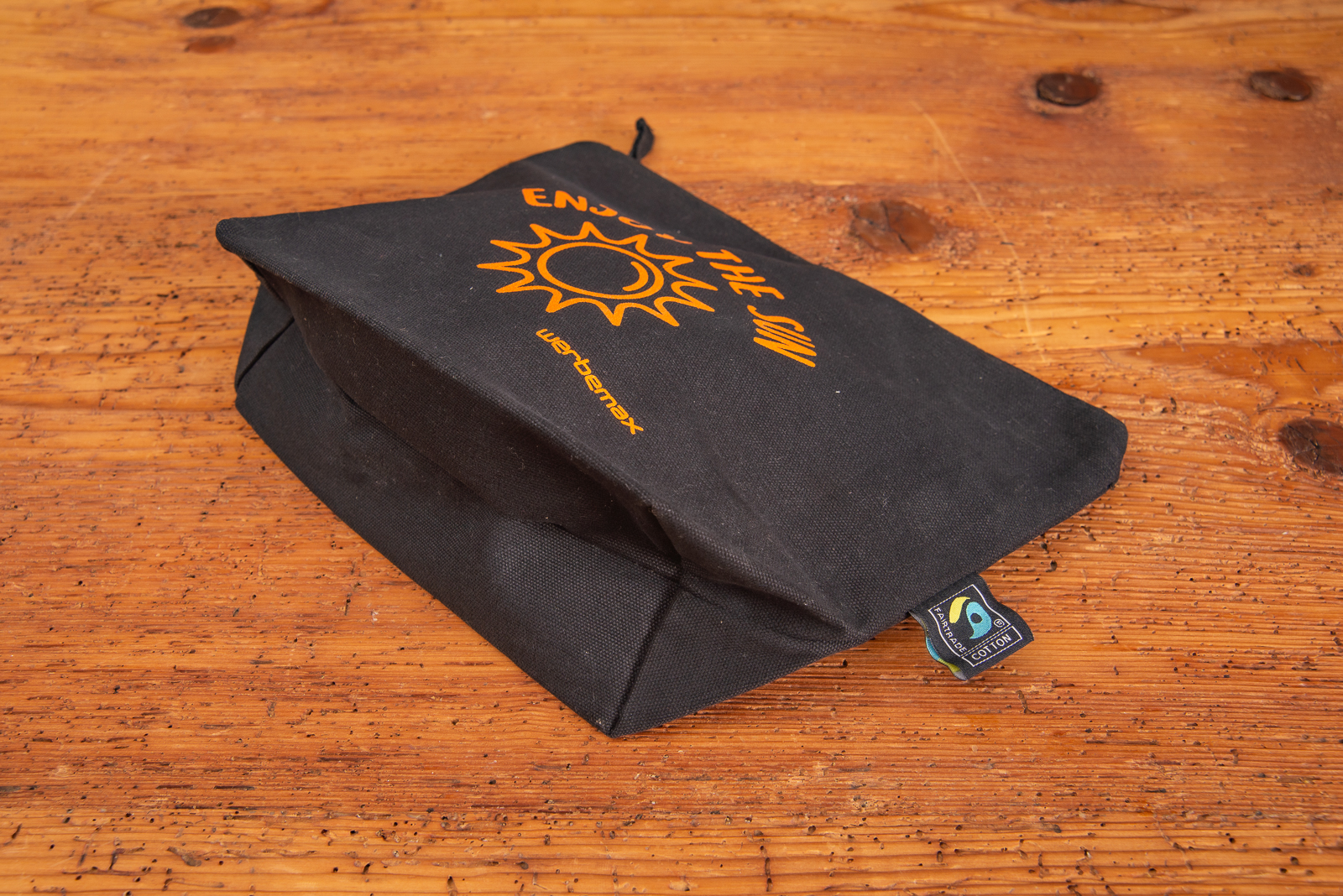 Schwarze Faitrade Kosmetiktasche mit Logoaufdruck in orange und Bodenfalte als Eigenwerbung f&uuml;r werbemax.