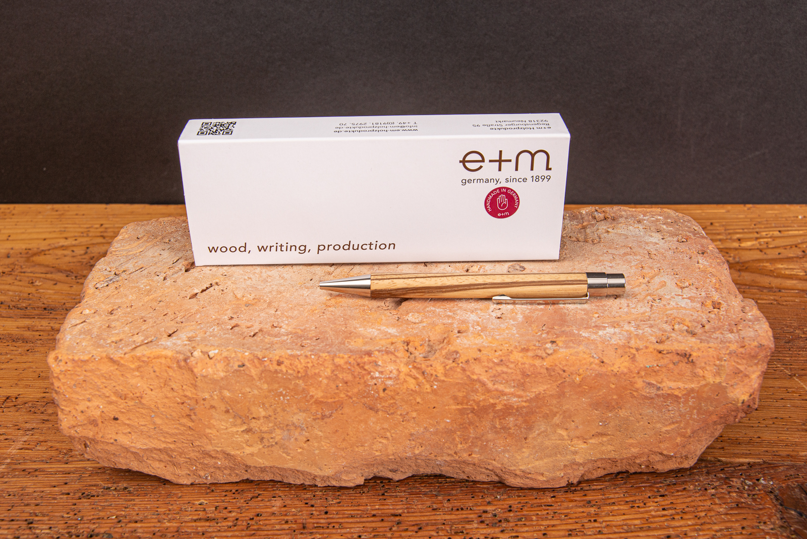 Nachhlatiger Kugelschreiber aus Edelholz in einer hochwertigen Geschenkverpackung mit Logodruck auf Backstein liegend