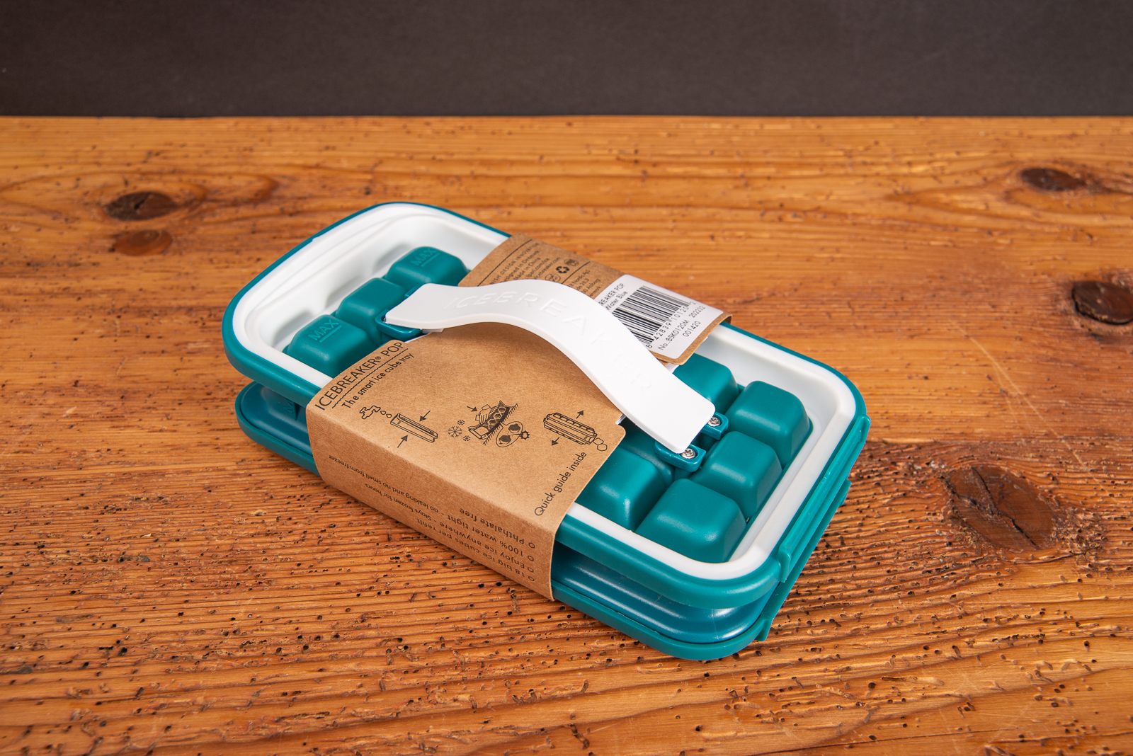 IceBreaker&reg; Pop in T&uuml;rkis geschlossen und auslaufsicher zur hygienischen Aufbewahrung von Eisw&uuml;rfeln mit Banderole auf Holztisch liegend.