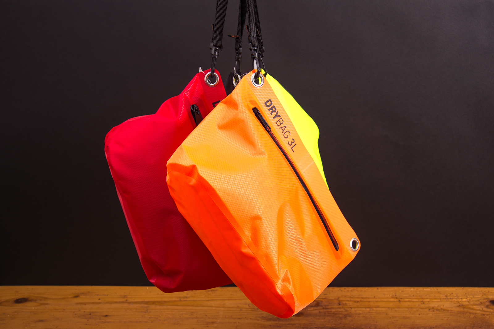 Drei bunte Drybags in Rot, Orange und Neongelb h&auml;ngend nebeneinander pr&auml;sentiert.