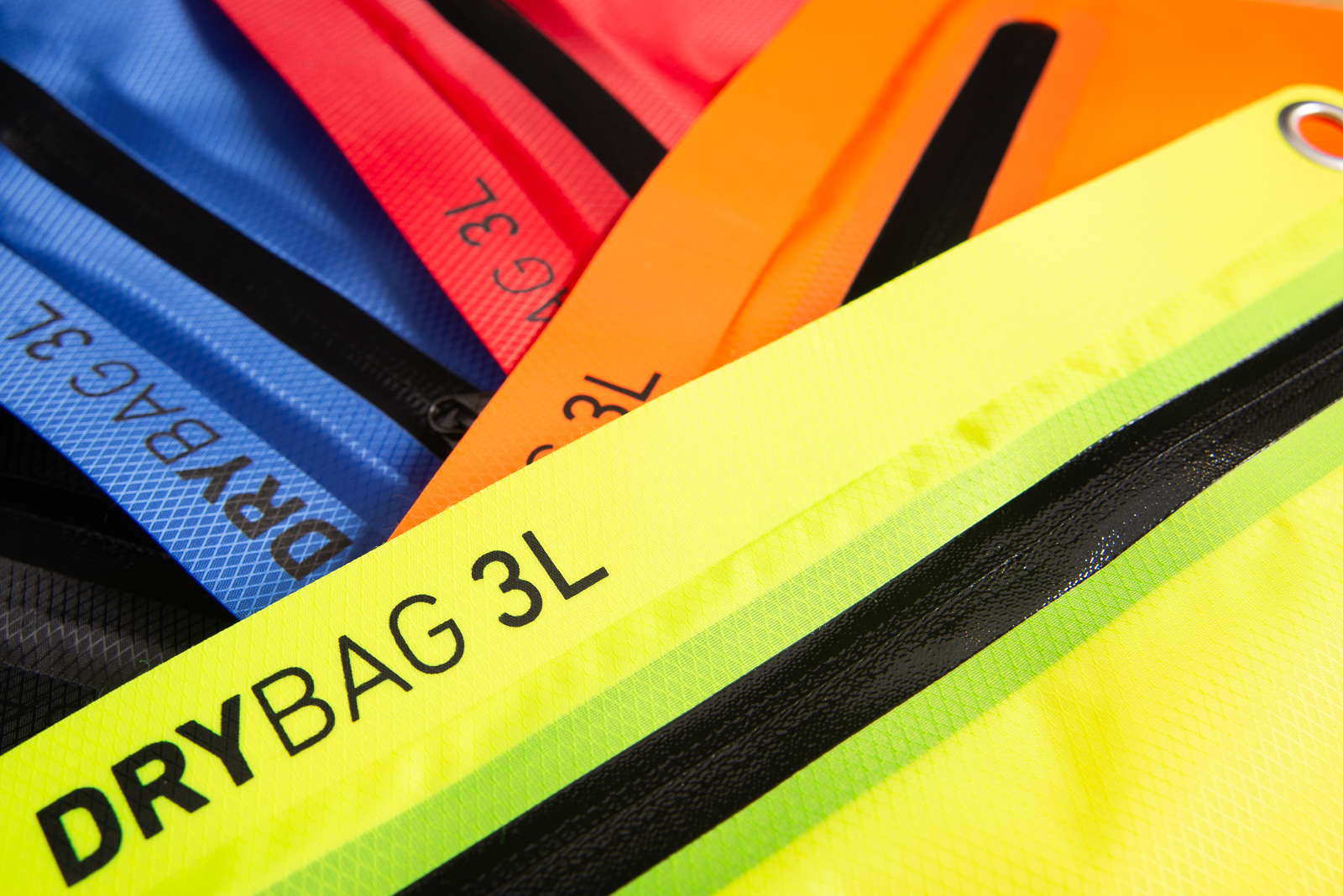 Nahaufnahme mehrerer Drybags 3L von Halfar in verschiedenen Farben mit Fokus auf wasserdichte Rei&szlig;verschl&uuml;sse.
