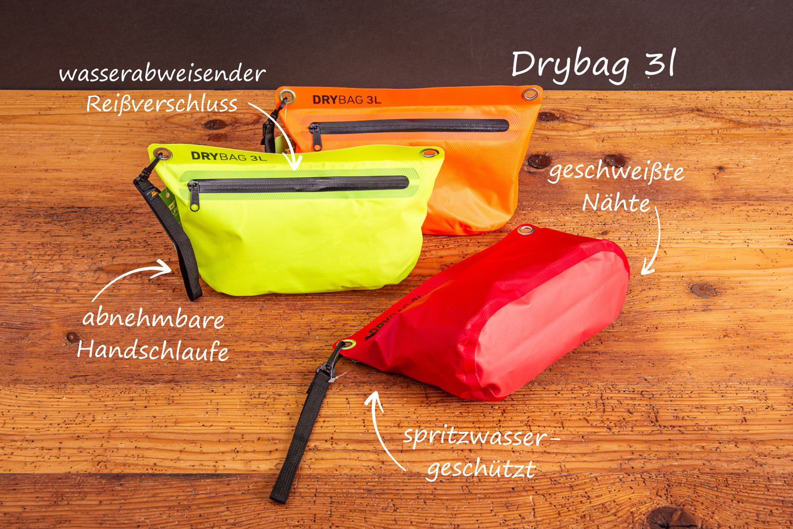 Drei Drybags mit erkl&auml;renden Texten zu Produktvorteilen wie spritzwassergesch&uuml;tzt, abnehmbare Handschlaufe und geschwei&szlig;te N&auml;hte auf Holztisch.
