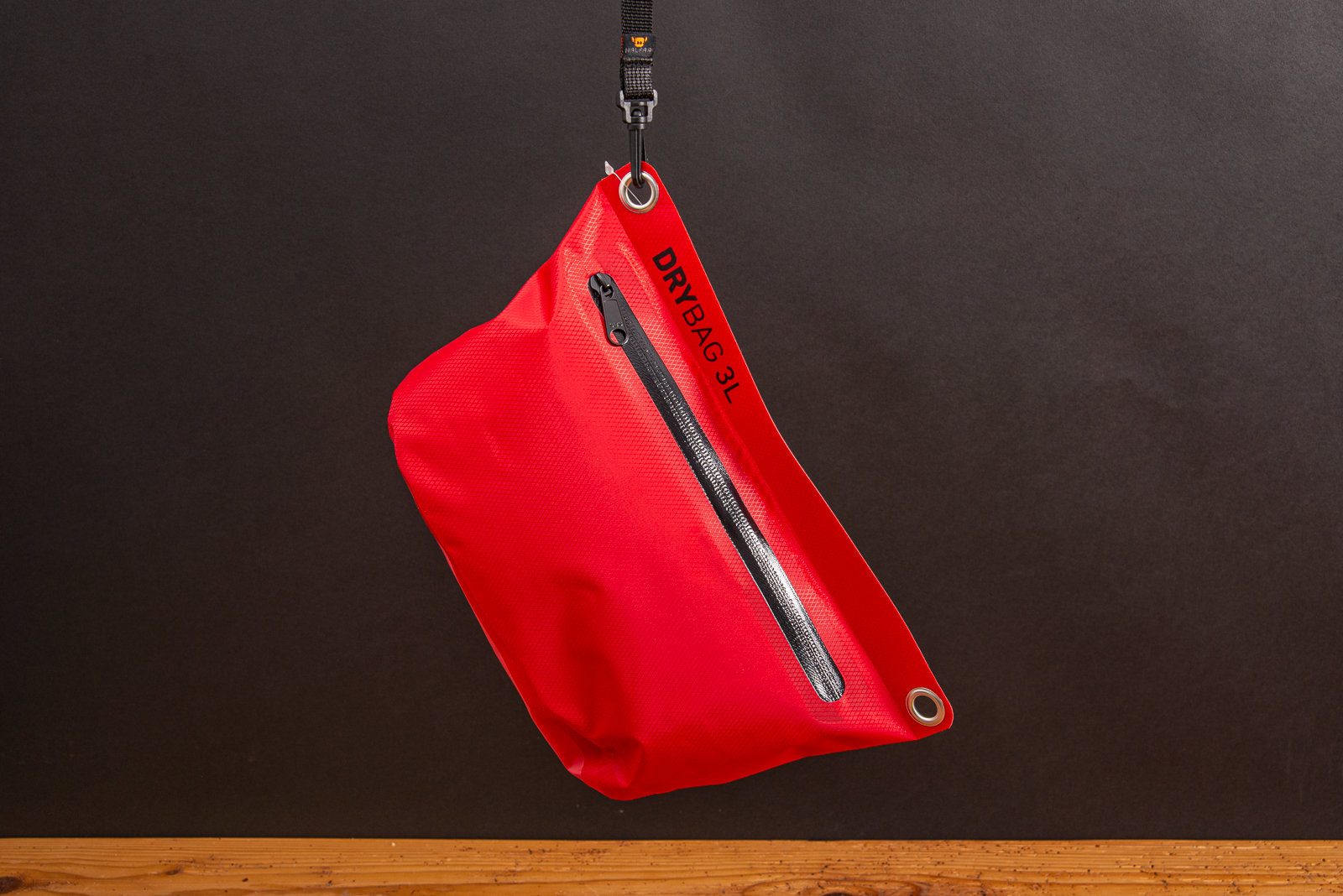 Rote Drybag 3L von Halfar h&auml;ngend vor schwarzem Hintergrund als Outdoor-Werbegechenk f&uuml;r Kunden und Mitarbeiter.