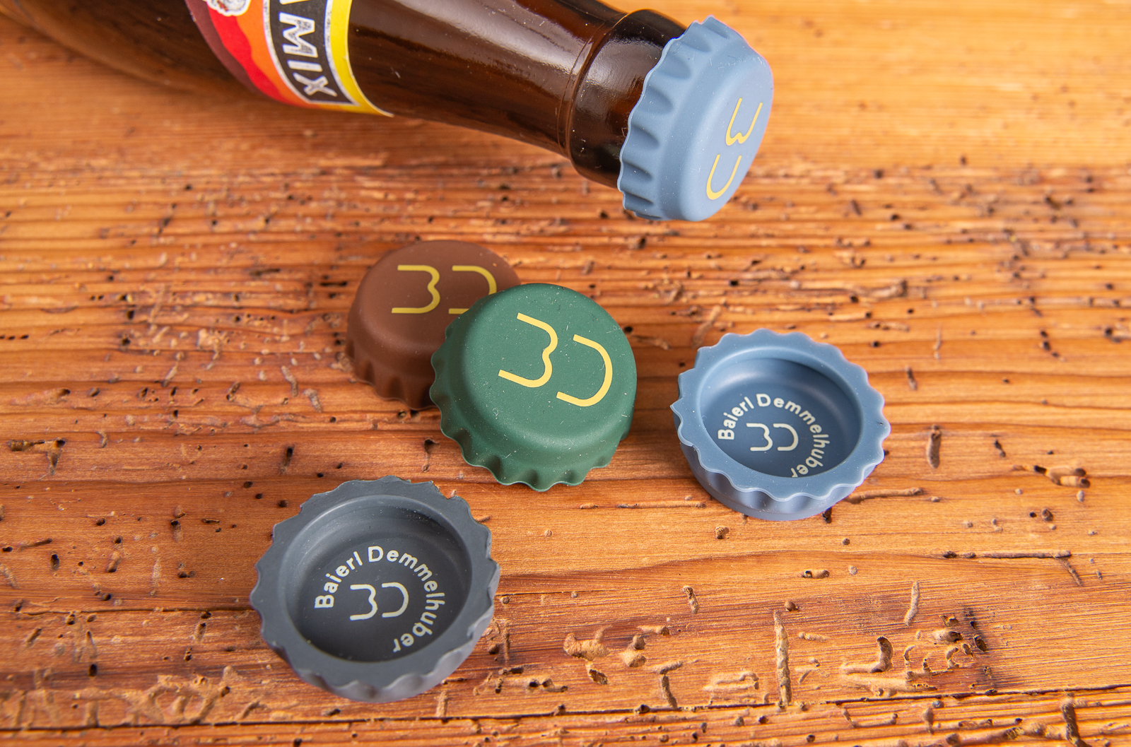 Verschiedene Korki Silikonkronkorken Referenz Baierl & Demmelhuber als Merch auf Holztisch liegend.