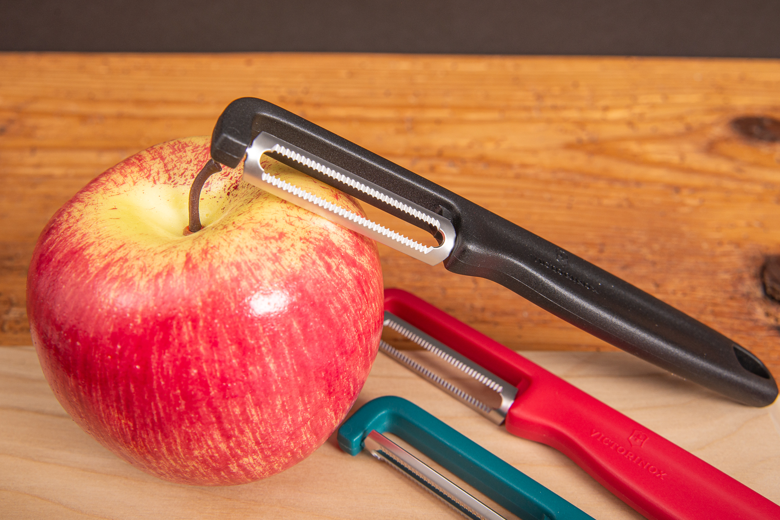 Victorinox Sparsch&auml;ler Iota in drei Farben mit Apfel auf Holzunterlage.
