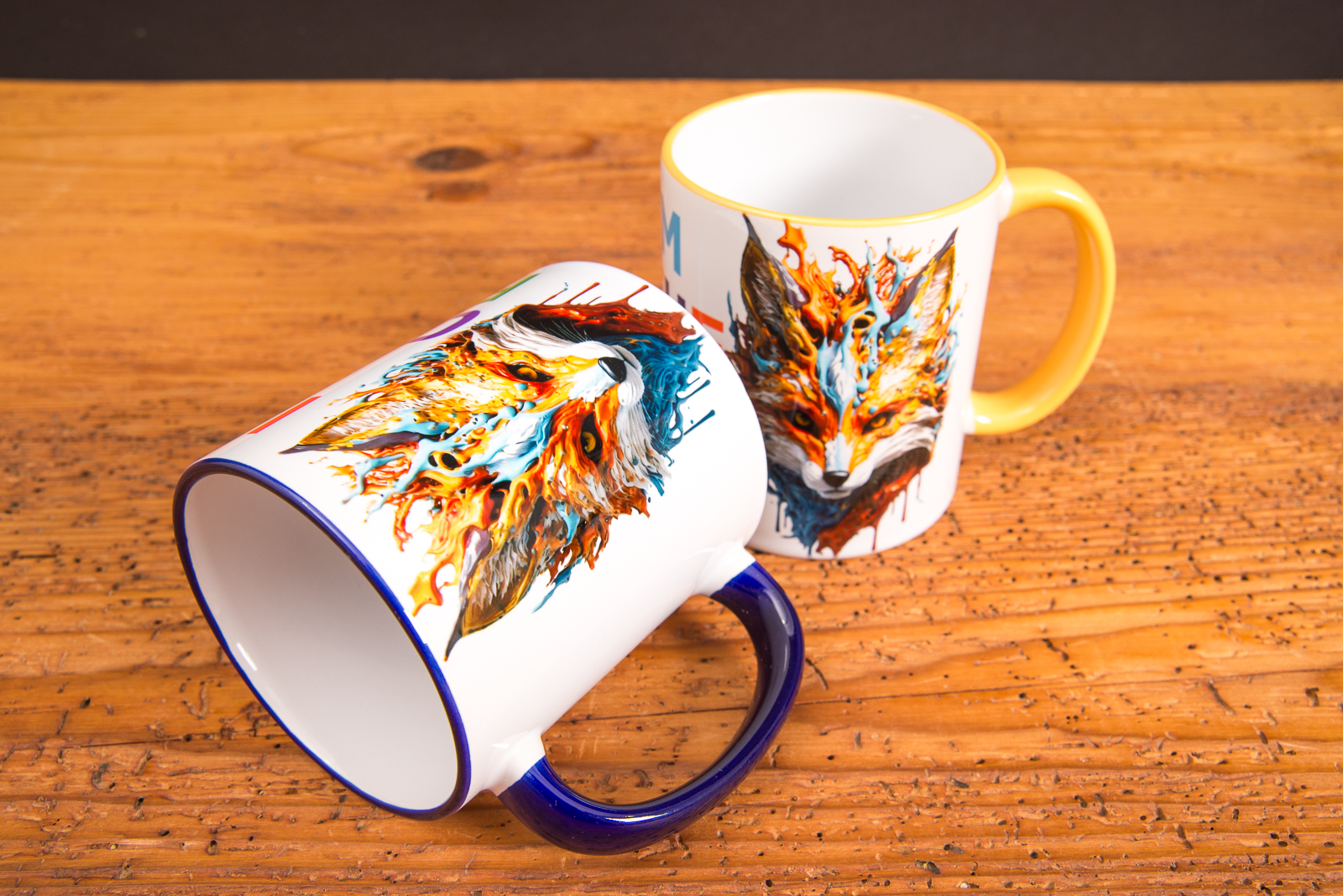 Zwei individuell bedruckte Keramik-Tassen mit farbigem Henkel und kreativem Fuchs-Motiv &ndash; hochwertige Werbeartikel Tassen von Werbemax auf Holztisch.