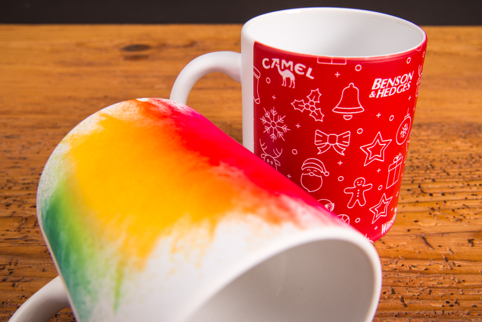 Nahaufnahme von zwei vollfl&auml;chig bedruckten Werbetassen mit Regenbogenverlauf und Weihnachtsmotiv &ndash; kreative Werbeartikel Tassen von werbemax.