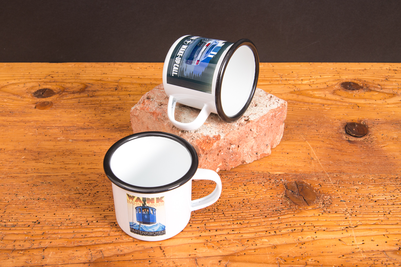 Zwei Emaille-Tassen mit Sublimationsdruck als individuelle Werbeartikel auf rustikalem Holztisch &ndash; Retro-Tassen von werbemax aus emailliertem Stahl.