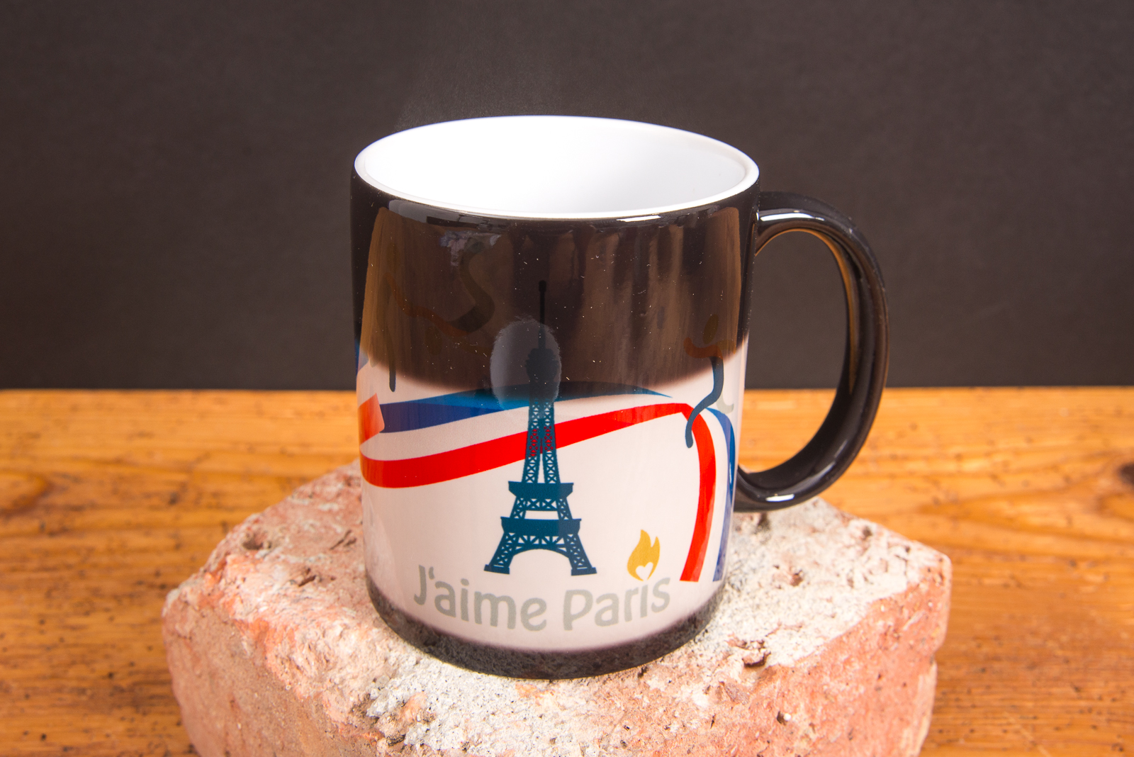 Thermotasse mit Farbwechsellack zeigt Eiffelturm-Motiv durch hei&szlig;e Bef&uuml;llung &ndash; Magic-Werbetasse von werbemax auf Backstein.