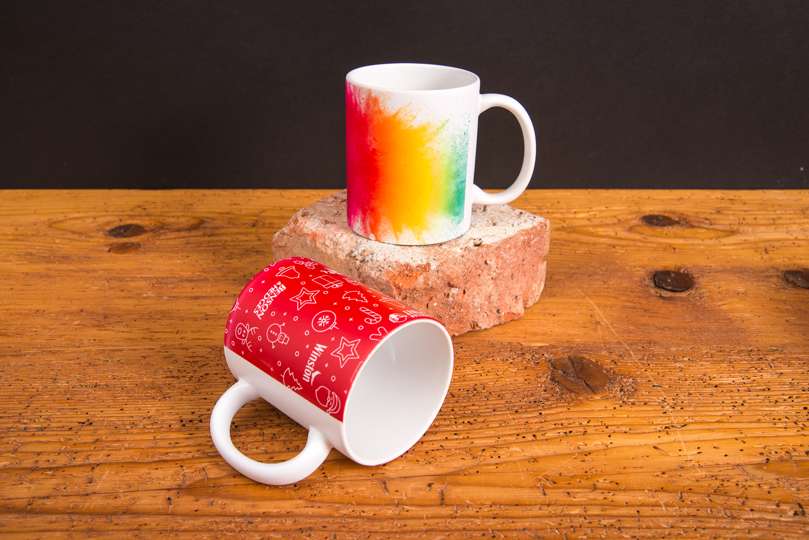 Zwei individuell bedruckte Tassen mit weihnachtlichem Design und Regenbogenverlauf &ndash; farbintensive Werbeartikel Tassen auf rustikalem Holzuntergrund.