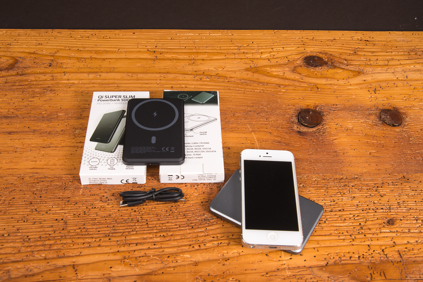 Wireless Powerbank mit Logo und MagSafe-Funktion, abgebildet mit Smartphone, Verpackung und Ladekabel auf einem Holztisch als Hochwertiges Incentiv im Merchandise.