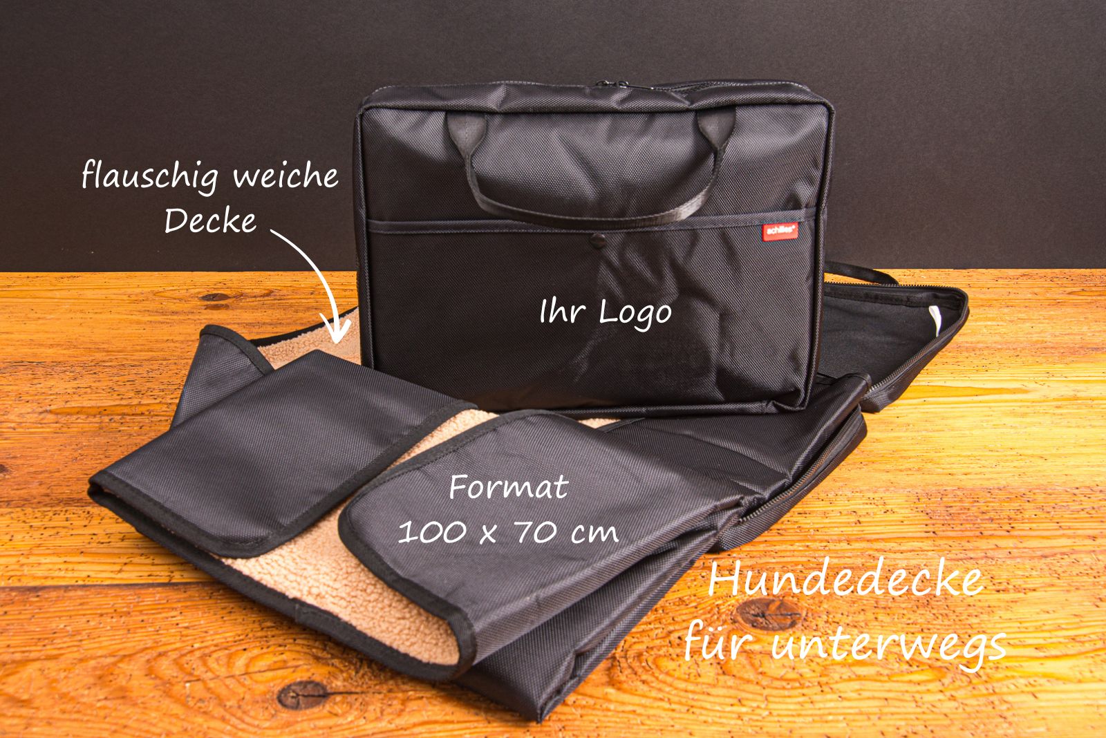 Hundedecke f&uuml;r unterwegs mit weicher Oberfl&auml;che und praktischer Tragetasche bedruckbar mit Logo als Werbegeschenk mit Bildbeschriftung auf Holztisch.