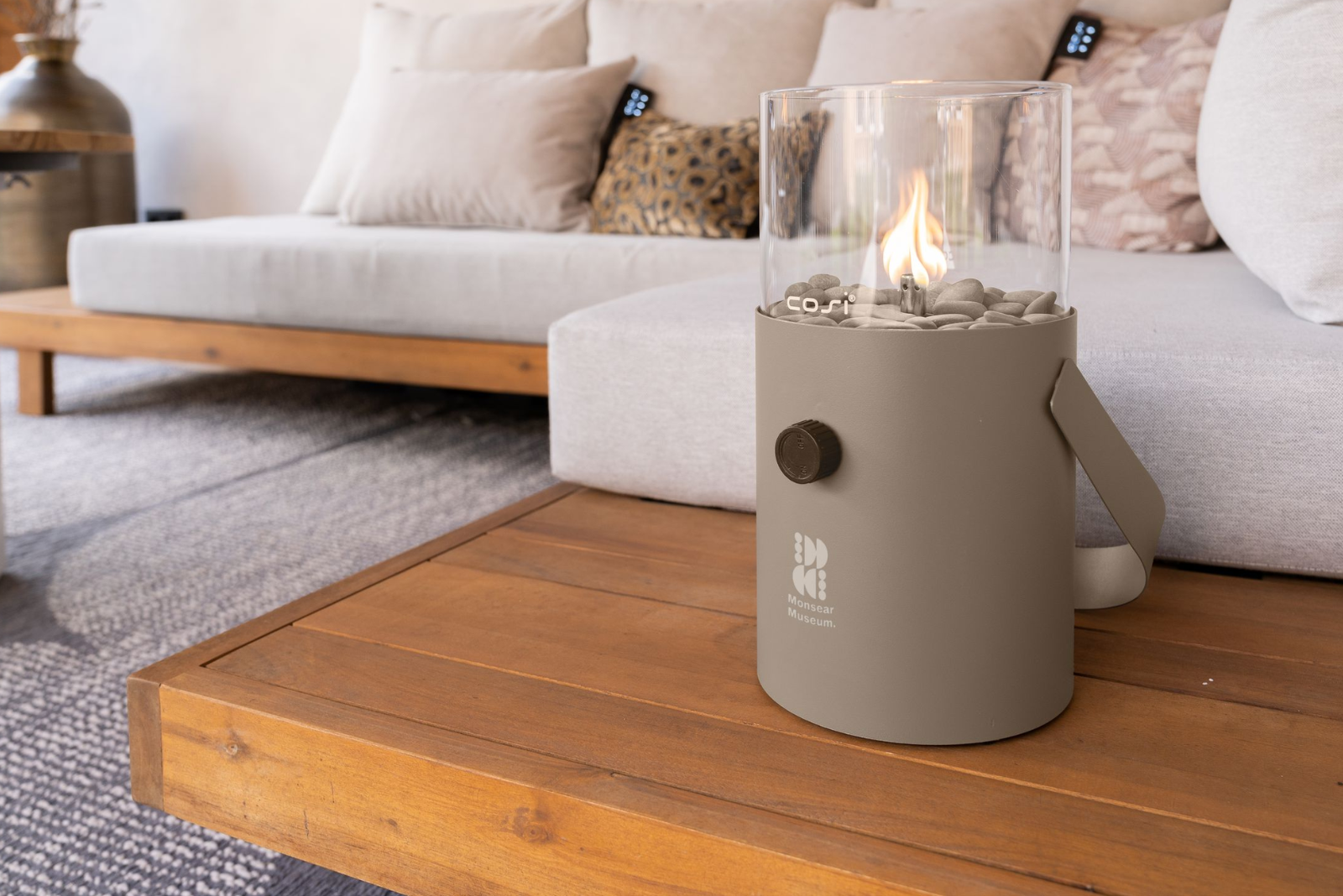 Elegante Gaslaterne der Marke Cosi als Tischfeuer auf einem Holztisch im modernen Wohnzimmer als hochwertiges Mitarbeitergeschenk.