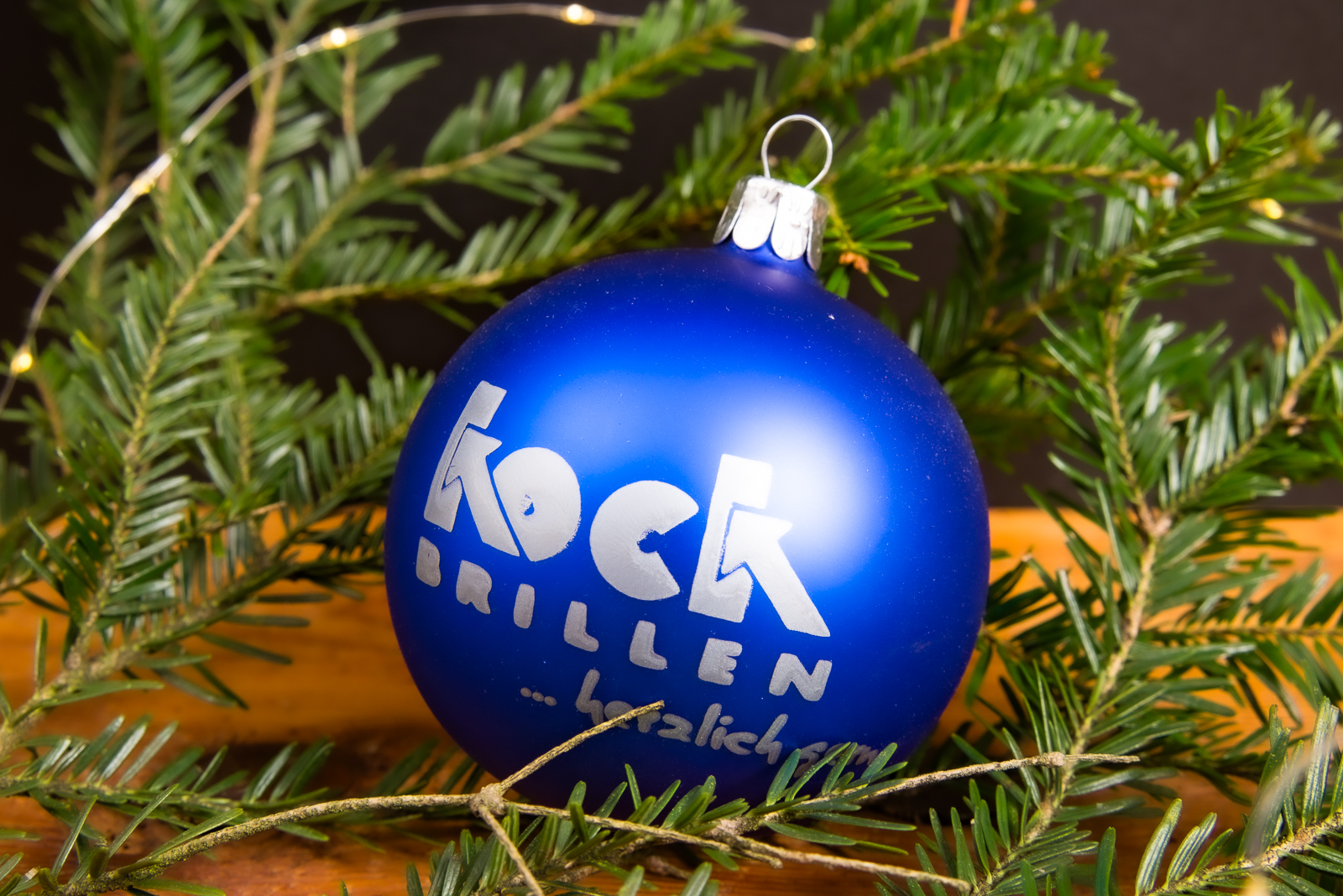 Blaue Weihnachtskugel mit wei&szlig;em Logo, dekoriert an Tannenzweigen als elegante Eventdekoration.