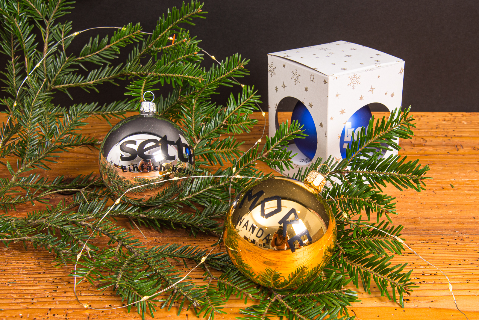Silberne und goldene Weihnachtskugeln mit Logo, dekoriert mit Tannenzweigen und Geschenkbox als indivduelles Werbemittel.