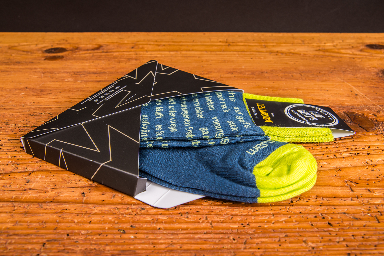 Bequeme Eigendesign-Socken mit Ihrem Logo in der versandf&auml;higen Mailingbox auf Holztisch.
