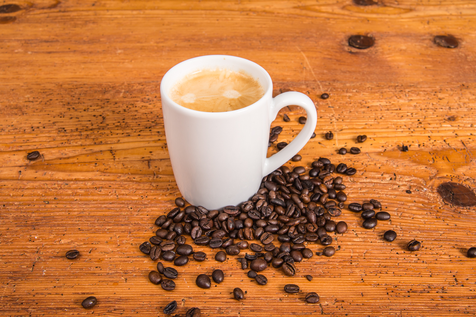 Wei&szlig;es Porzellantasse von SND mit frischem Kaffee und Kaffeebohnen auf Holztisch als hochwertiger Werbeartikel.