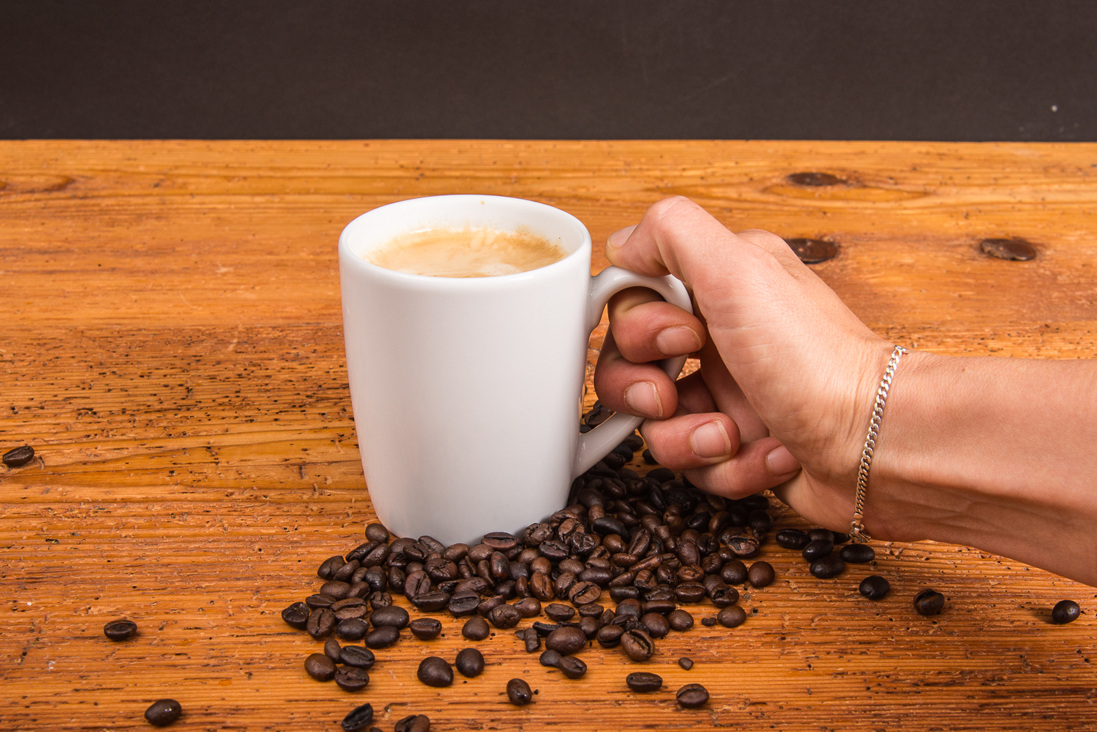 Person h&auml;lt SND Porzellan Tasse mit Kaffee und in Kaffeebohnen stehend mit Logo Druck als Werbeartikel einsetzbar