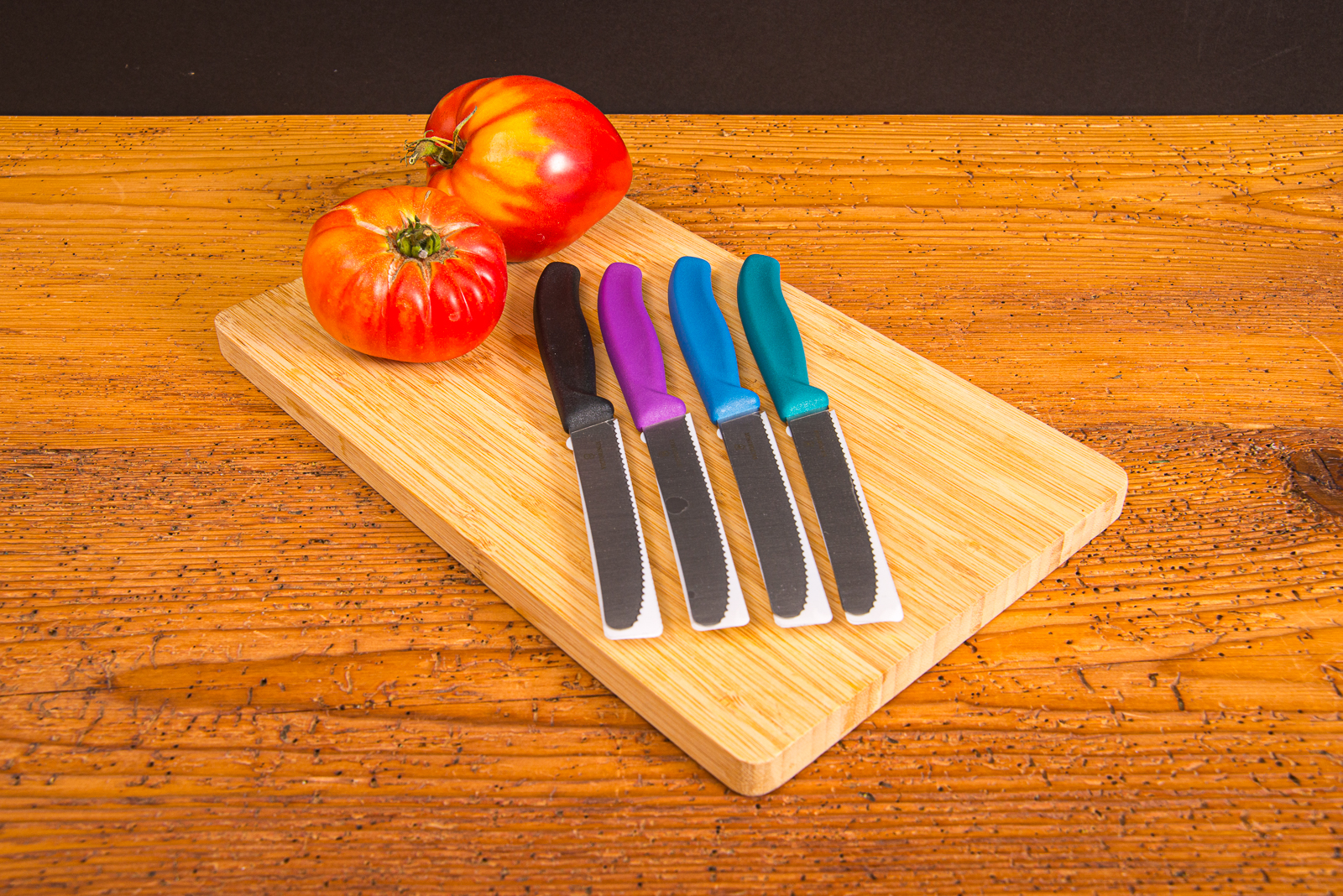Bunte Victorinox Tomatenmesser auf Schneidebrett mit frischen Tomaten &ndash; langlebige Messer mit Logogravur.